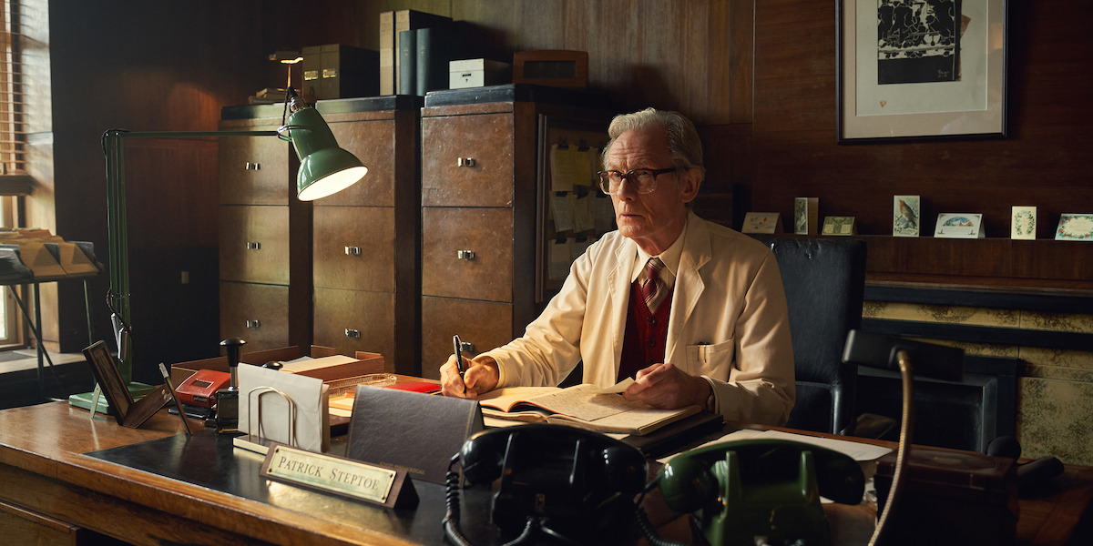 Patrick Steptoe (Bill Nighy) sits at a desk lit by a lamp