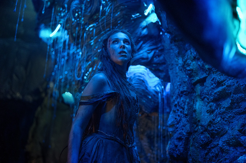 Millie Bobby Brown as Elodie in a surrounded by blue light in a cave.