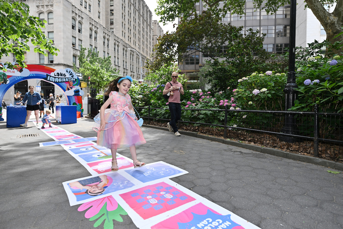 Young girl in a pink dress playing hopscotch in a park