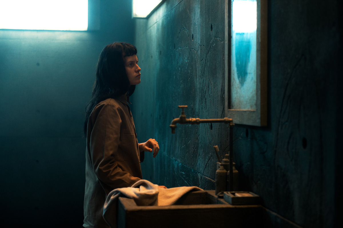 In a still image from ‘The Platform 2,’ Milena Smit as Perempúan stands beside a sink in a prison cell while looking into the mirror.