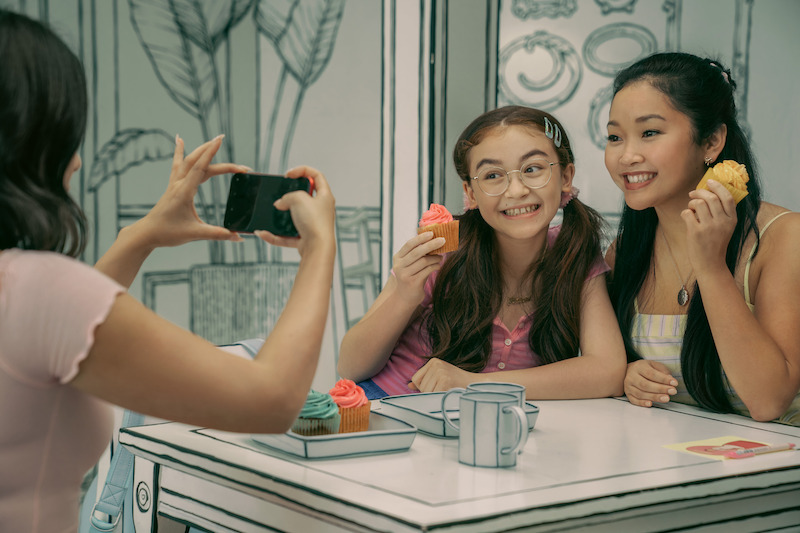 Anna Cathcart as Kitty, Lana Condor as Lara Jean, and Janel Parrish as Margot take pictures at a cafe.