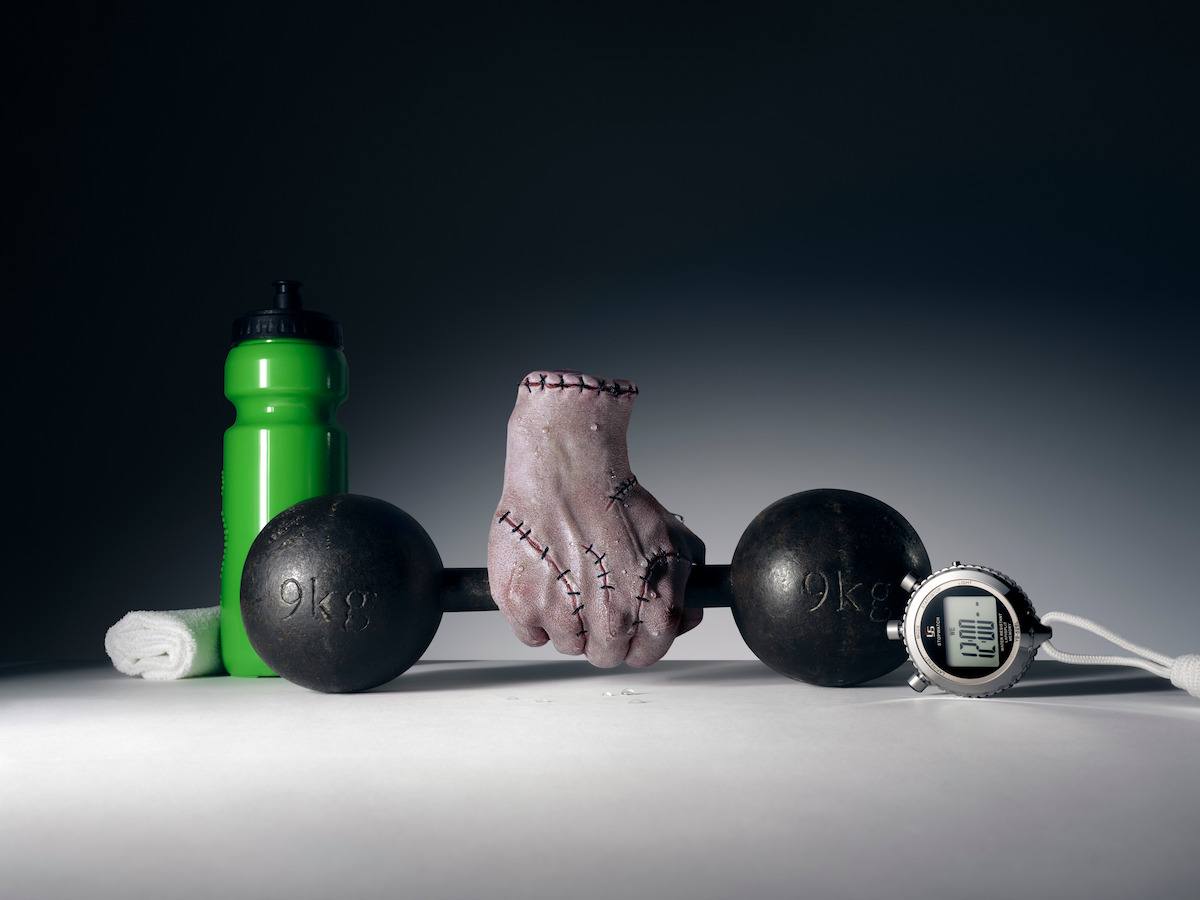 Thing holding a 9kg dumbbell next to a water bottle, towel and stopwatch.