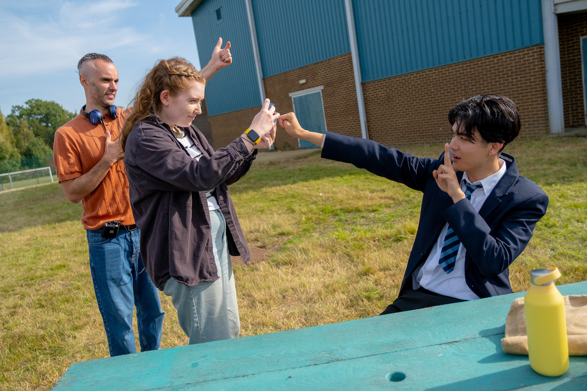 Behind the scenes image of Alice Oseman taking a photo of William Gao as Tao on the set of Season 3 of ‘Heartstopper’