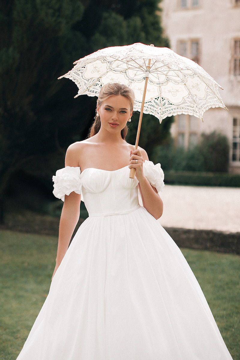 Woman in bridal dresses poses and looks off into the distance.