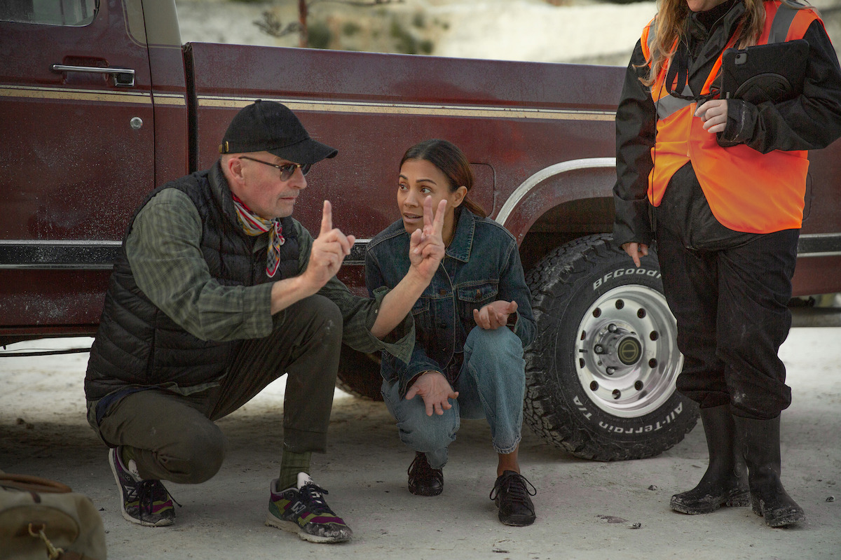 Jacques Audiard and Zoe Saldaña behind the scenes squat by a old-timey car.
