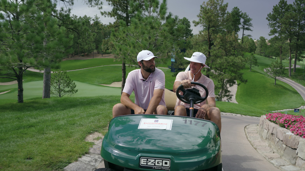 Scottie Scheffler and Ted Scott ride in a golf cart together.