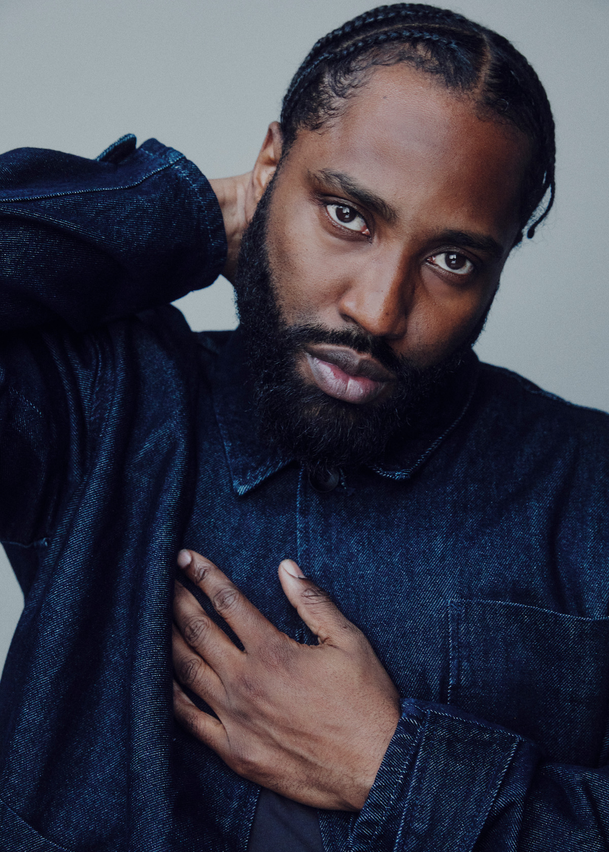 John David Washington wears a dark blue long-sleeved and holds his hand to his heart.