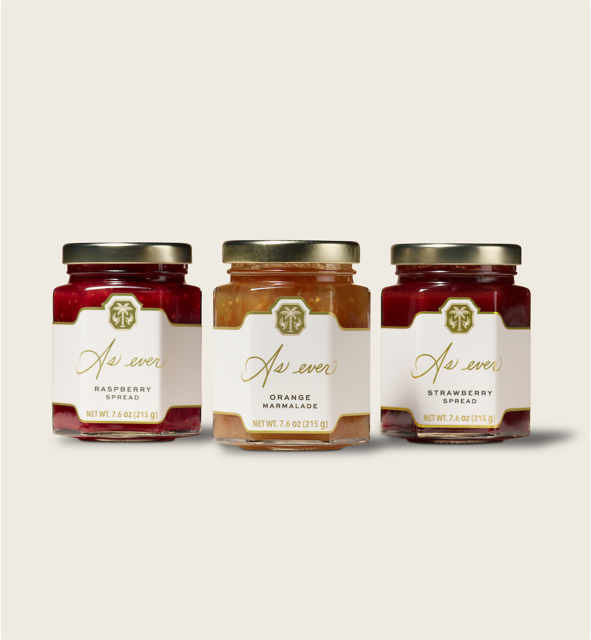 Three glass jars of fruit spreads (raspberry, orange marmalade, and strawberry) sit side by side on a plain, light background; modern, clean labels create a fresh, inviting mood.