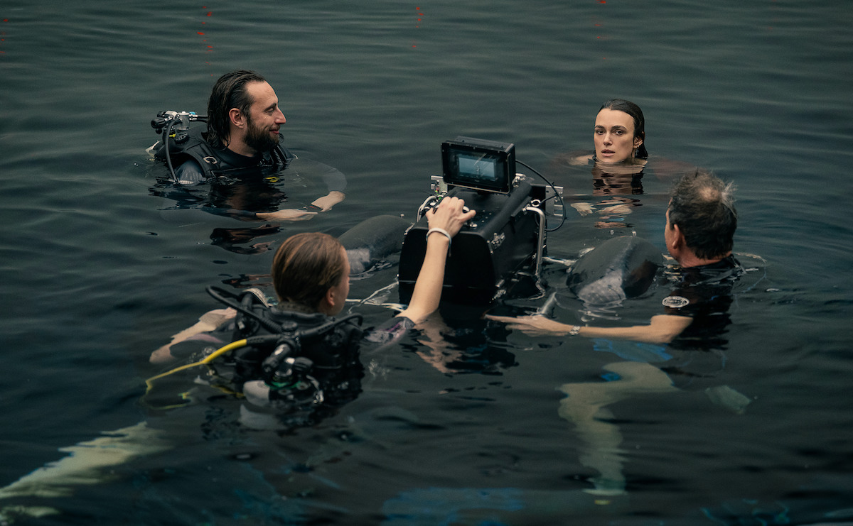 Four people in scuba gear are filming in dark water with a camera; the mood is serious and professional, suggesting a behind-the-scenes look at an underwater movie or TV production.