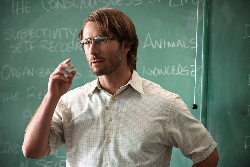 Gary Johnson (Glen Powell) wears a short-sleeved shirt and glasses, standing in front of a blackboard.