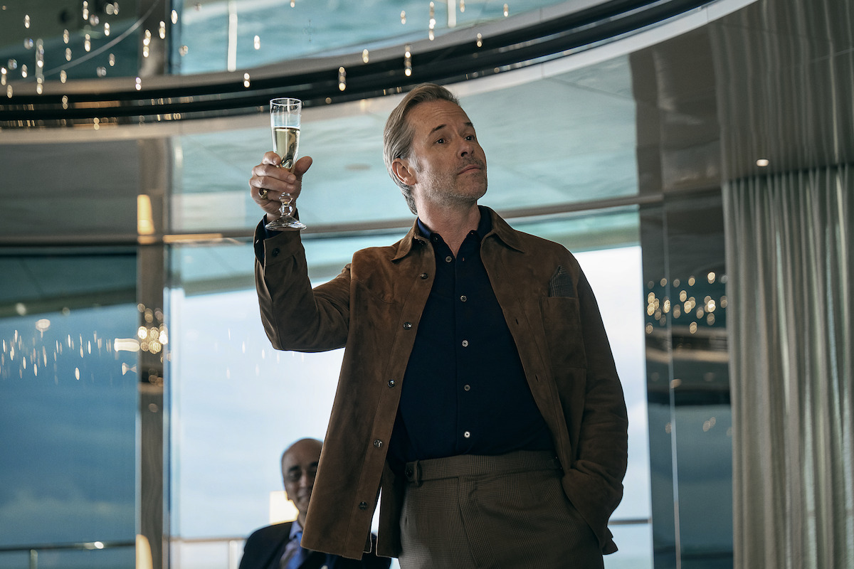 Guy Pearce holds up a flute of champage while giving a toast to a group of people aboard a yacht.