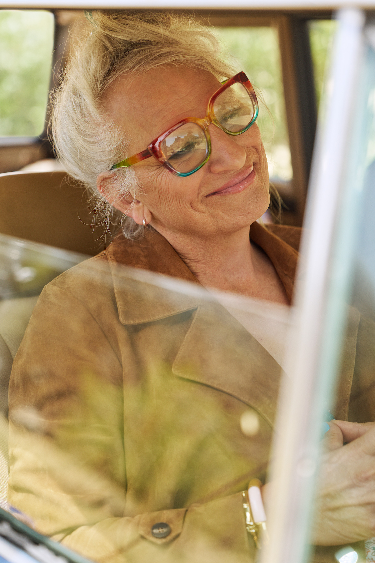 Harper Steele smiles slightly in a retro car. She wears cool big glasses and can be seen through a half-open window.