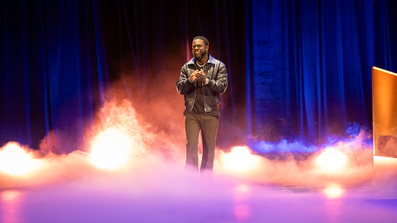 Kevin Hart stands on stage as fog surrounds him.