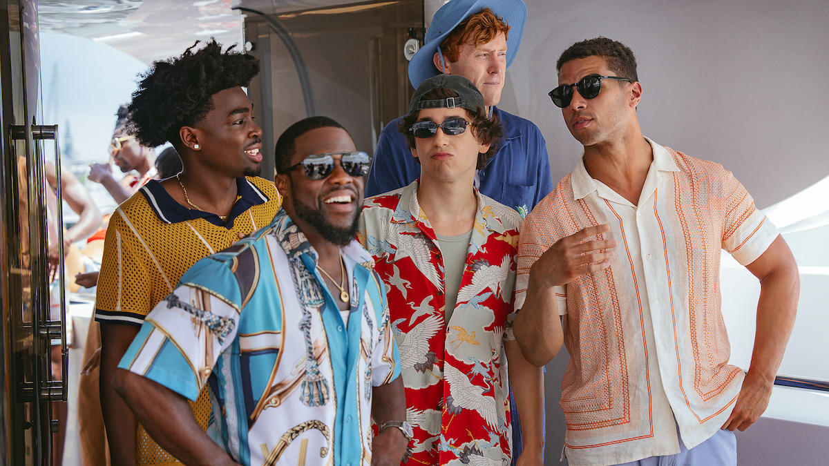 Five men in colorful summer shirts and sunglasses talking and laughing on a yacht, bright daylight, casual vacation atmosphere.