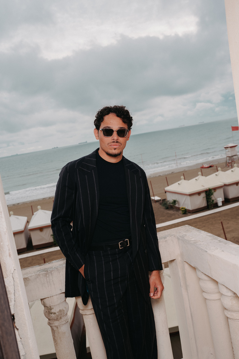 Anthony Ramos wears sunglasses and a black jacket on a balcony in Venice.