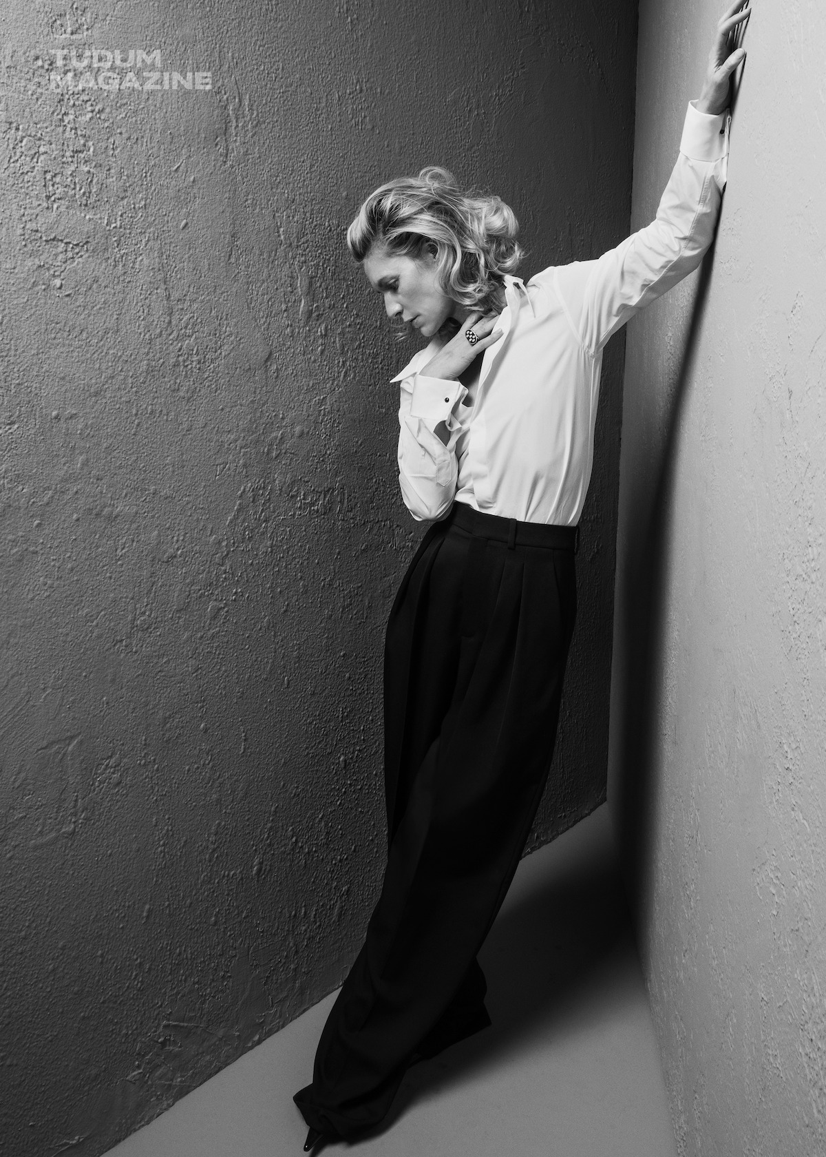 Claire Danes wears a white blouse and a black pair of pants, looking away from the camera.