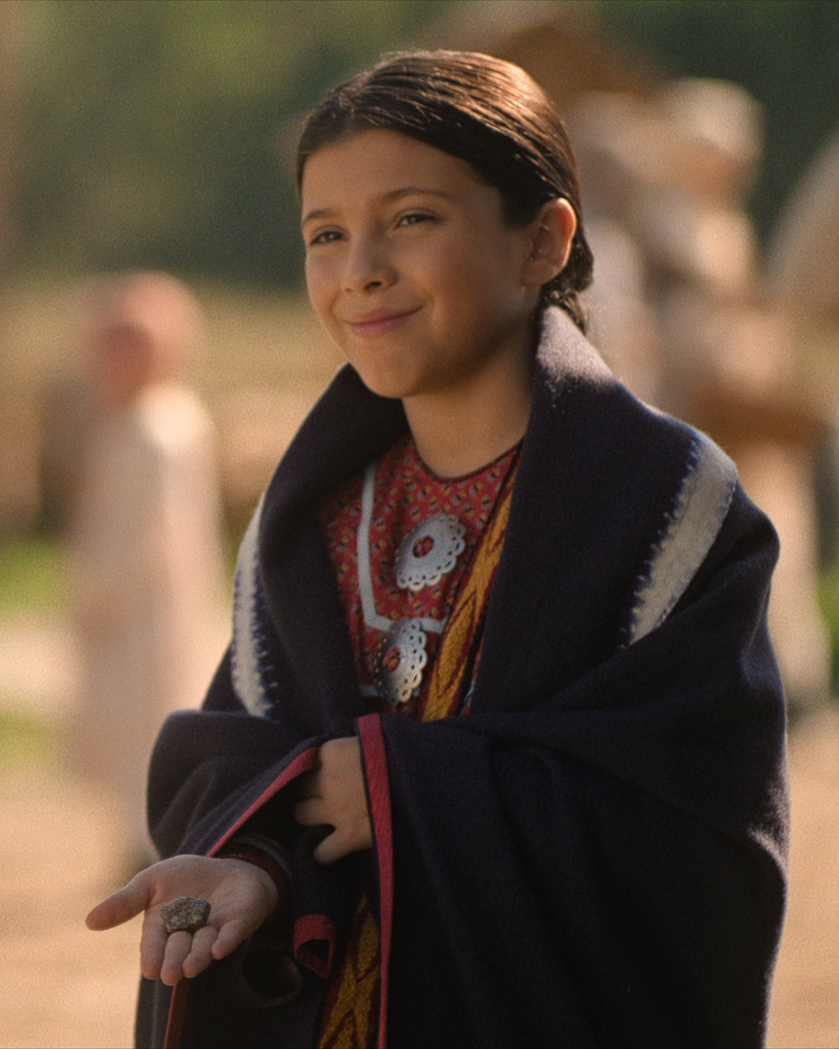 A young girl smiles and holds her hand out.