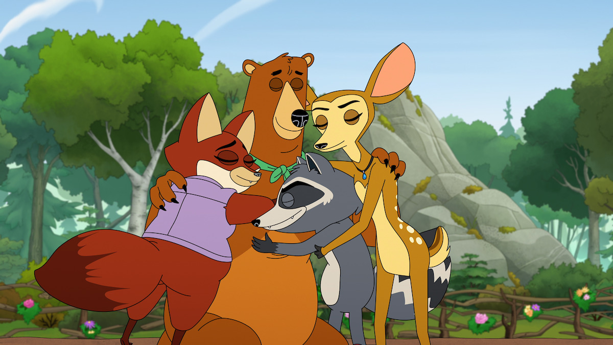 Four cartoon animals—a fox, bear, raccoon, and deer—share a group hug in a lush forest clearing with trees, rocks, and clear skies in the background, conveying friendship and warmth.