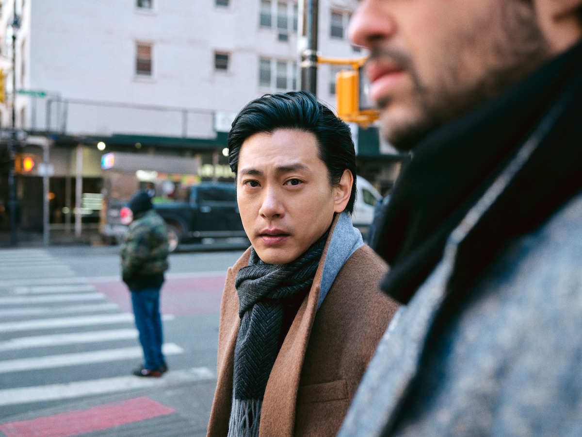 On the street, Teo Yoo looks into the camera with Noah Centineo in the foreground.