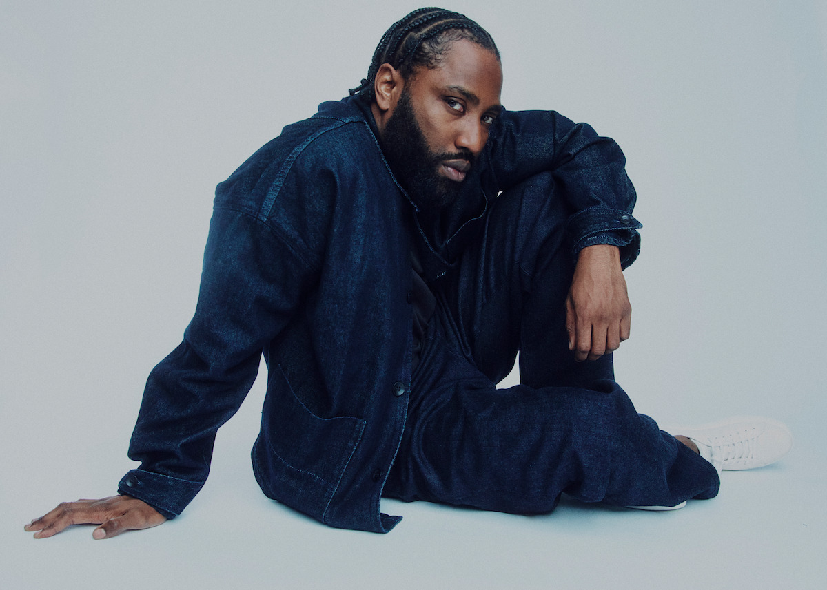 John David Washington wears all navy and poses against a grey background.