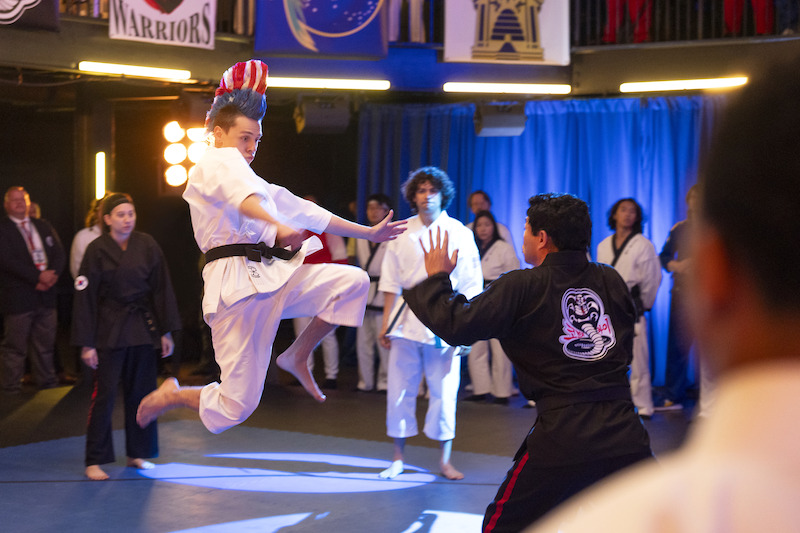 Jacob Bertrand as Eli 'Hawk' Moskowitz jumps in a kicking position in a competition in Season 6, Part 2 of 'Cobra Kai'