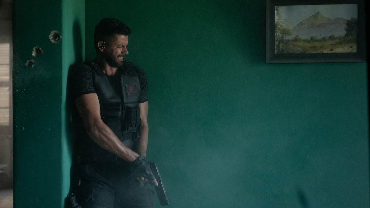 Tim Theron stands in a corner holding a gun in a still image from the film ‘Heart of the Hunter.’