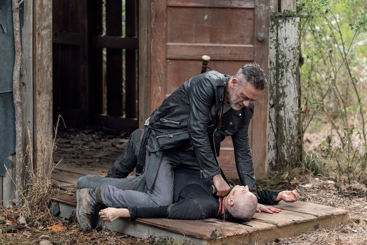 Negan sitting on top of someone holding them down. 