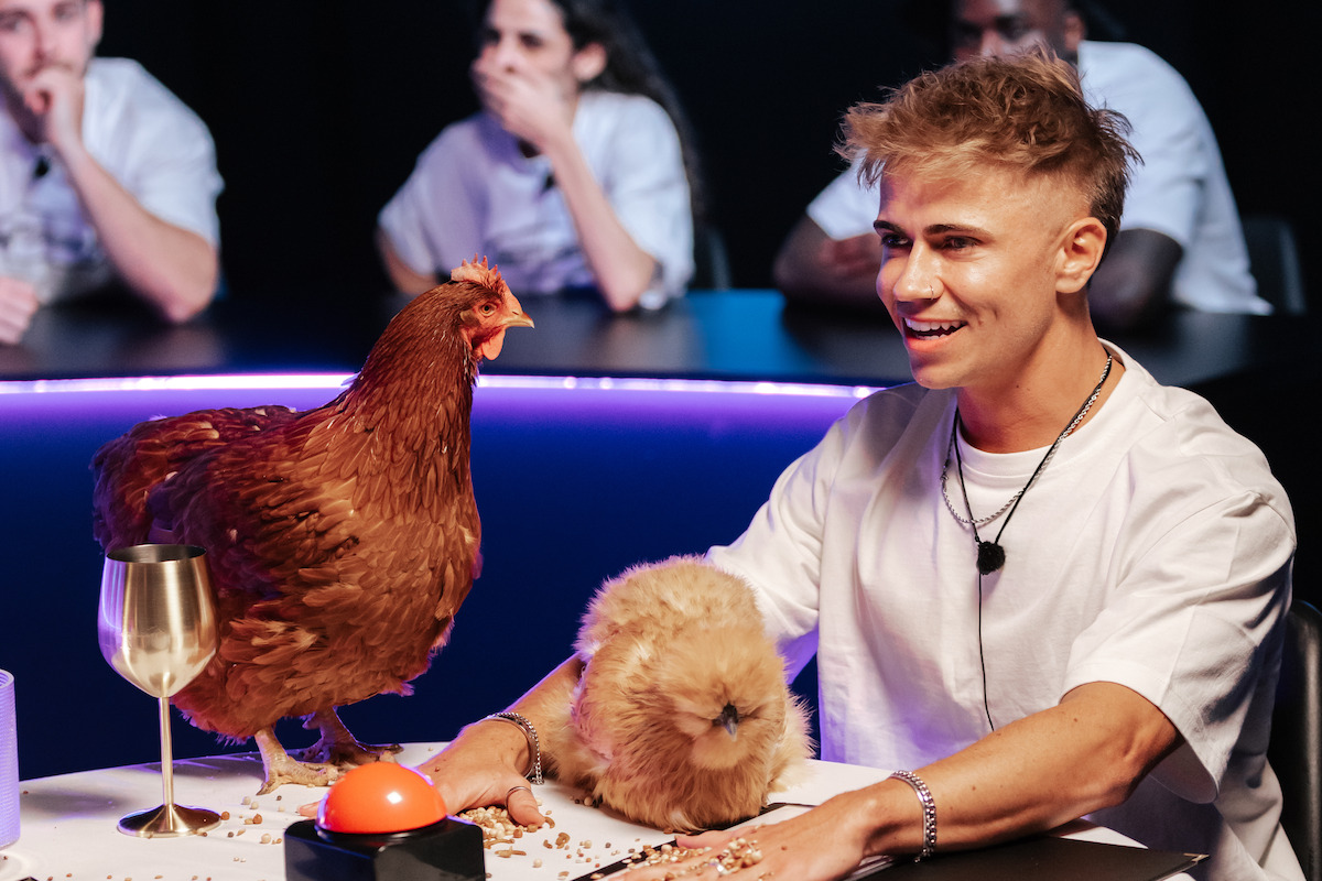 A guy sits at a table with a buzzer and two chickens in ‘Inside’ Season 2.