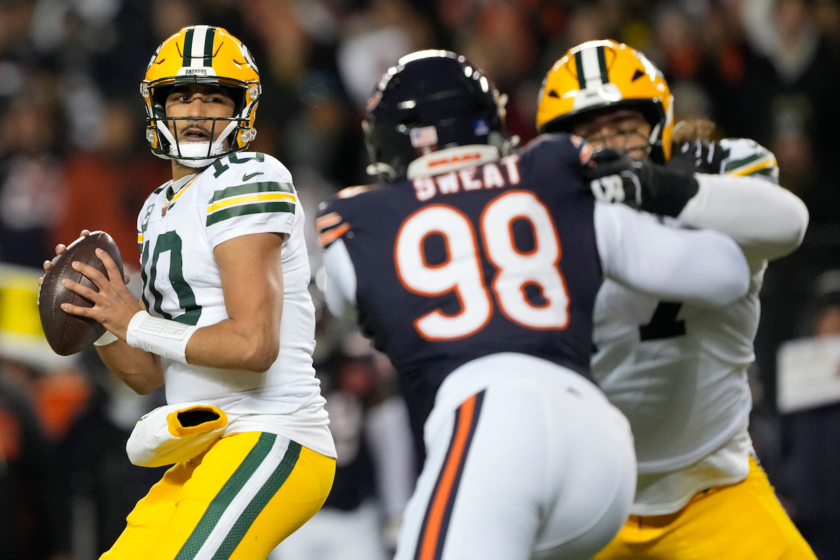 Green Bay Packers quarterback looks to throw as Chicago Bears defender rushes, Packers offensive lineman blocks during a night NFL football game in a stadium full of fans.