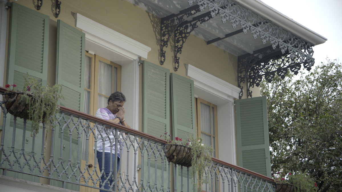 A man standing on an upper balcony in New Orleans praying.