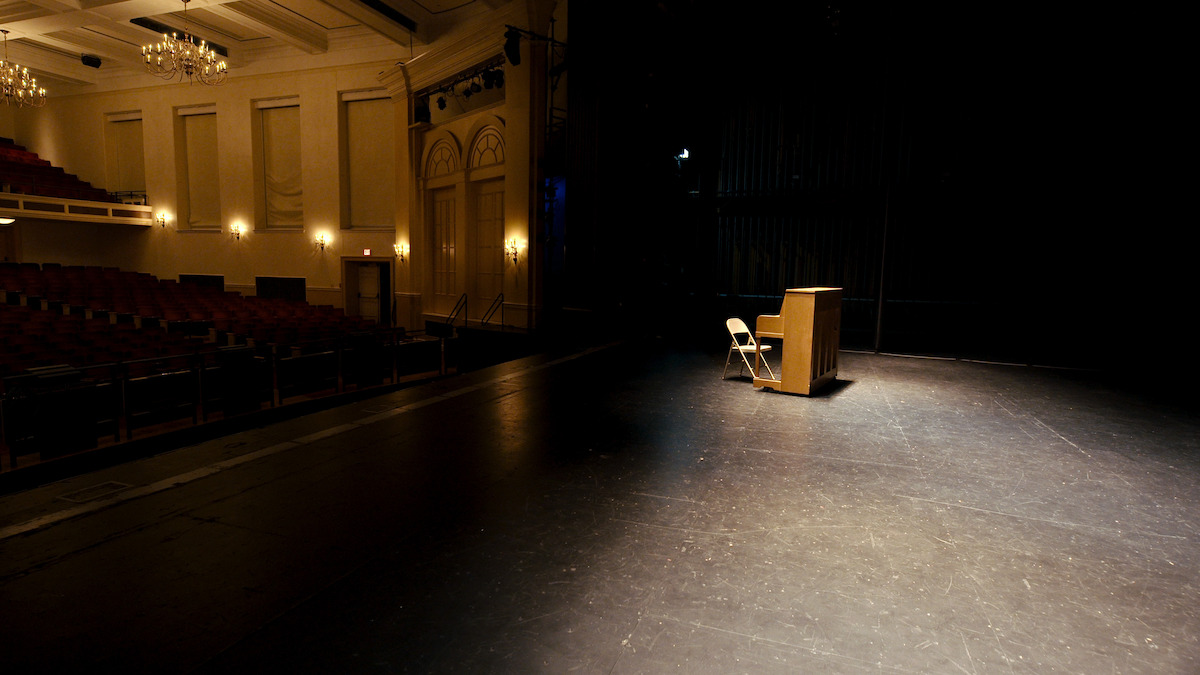 An piano sits on an empty stage.