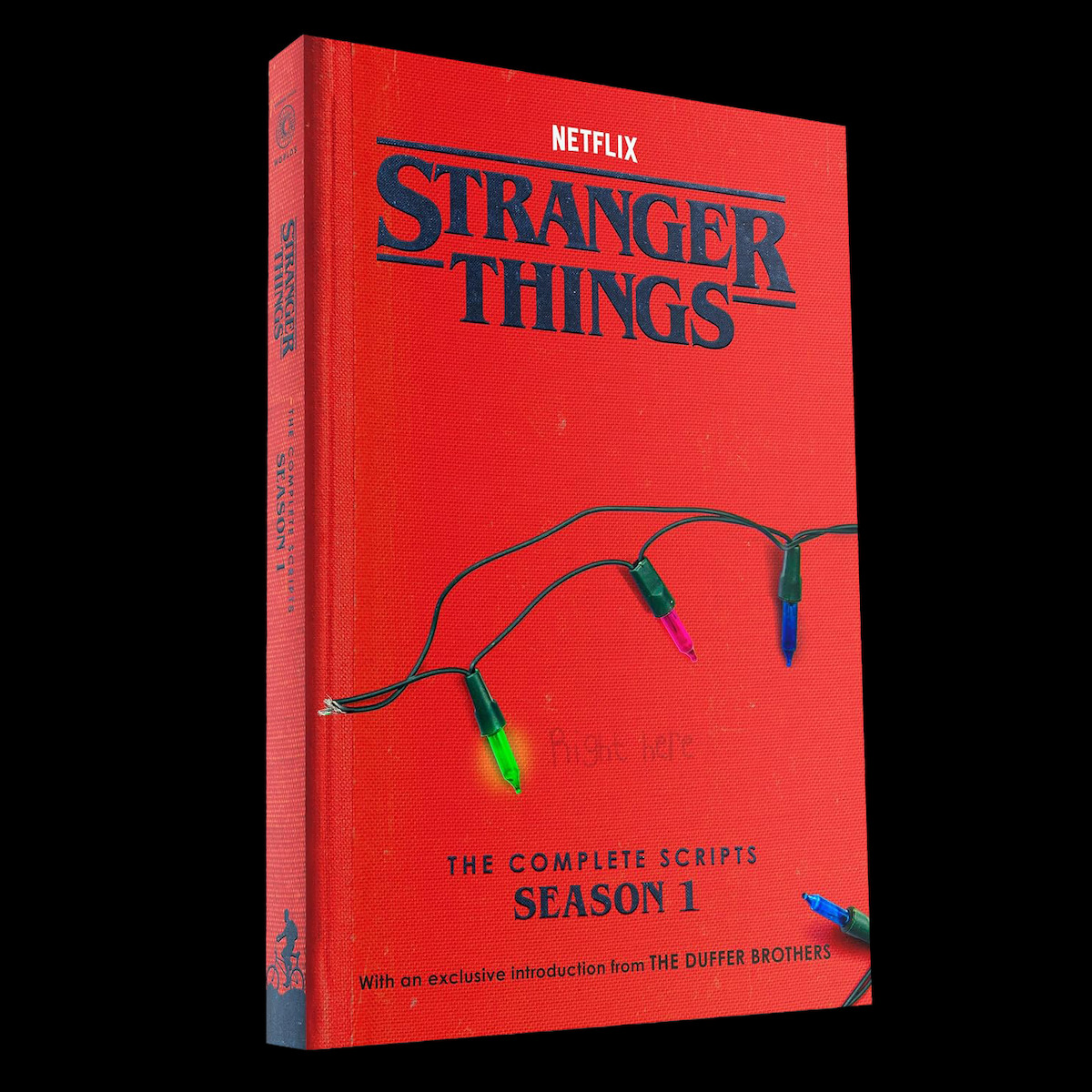 Red ‘Stranger Things: The Complete Scripts Season 1’ book by Netflix, features Christmas lights on the cover, set against a black background. Mysterious, nostalgic mood referencing the show's themes.