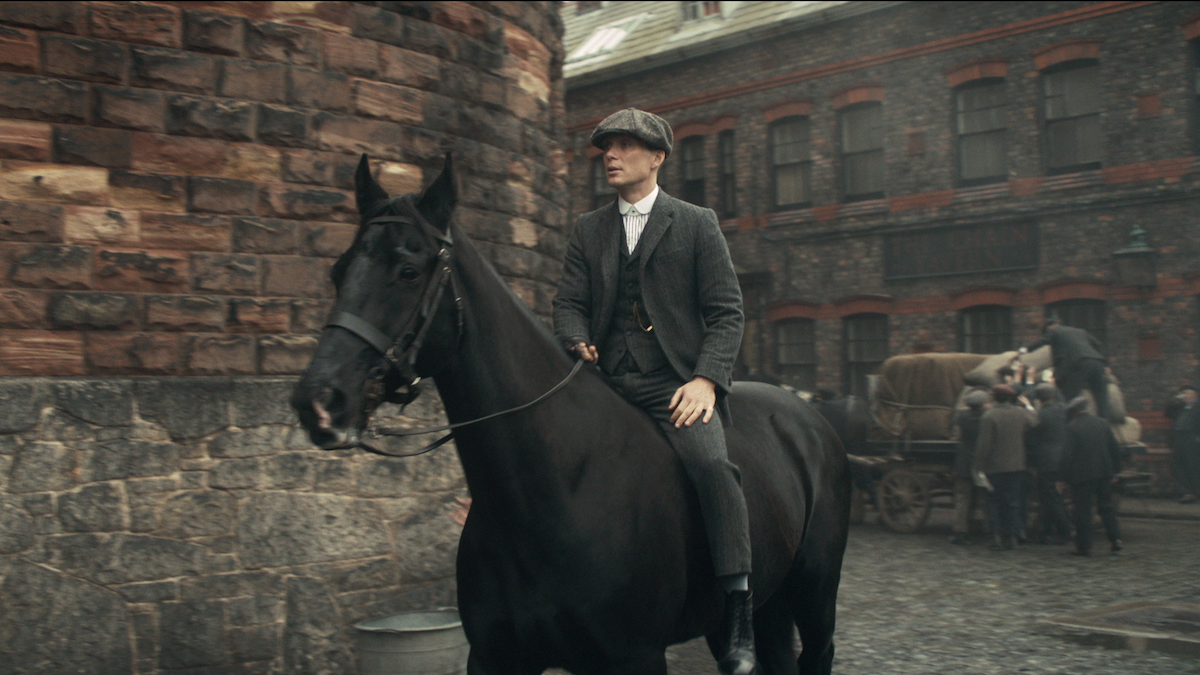 A man in a suit and hat is mounted on a horse in the middle of a city street. Both look into the distance.