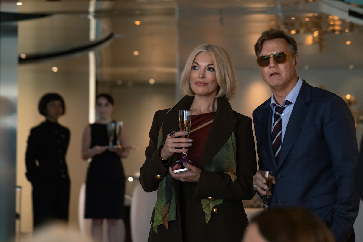 Hannah Waddingham holds a champagne flute next to David Morrissey in sunglasses in formal clothes.