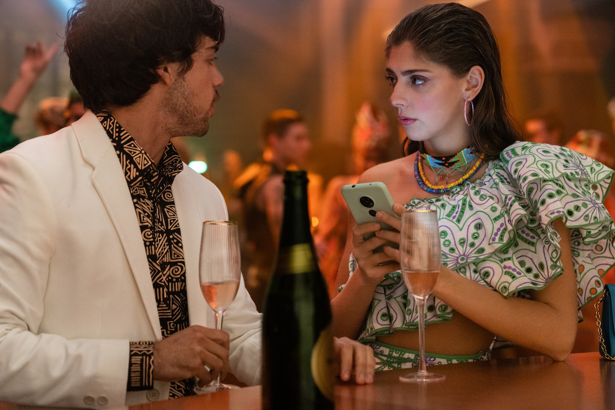 Alex Pastrana as Raúl Carmen Arrufat as Sara stand together at a bar in Season 7 of ‘Elite.’