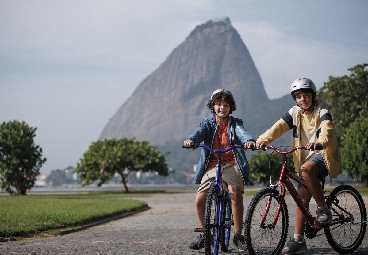 Enzo Diniz as Marcos and Theo de Almeida as Mateus ride bikes in a park in an image from the series ‘Desperate Lies.’