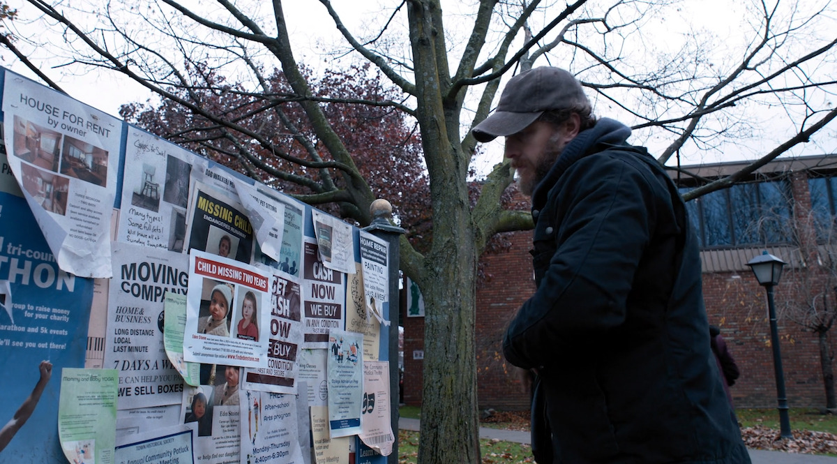 A man staring at a bulletin board filled with missing posters.