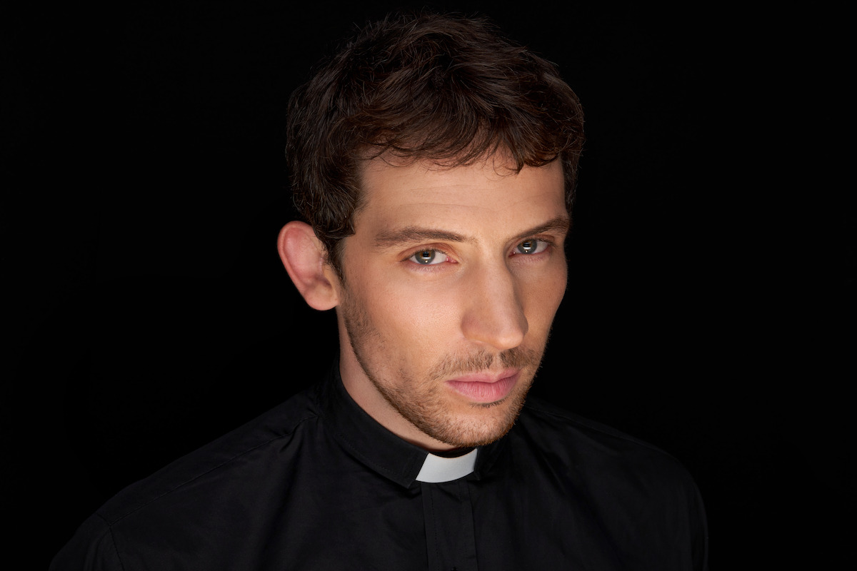 Young man wearing a black clerical shirt and white collar, looking serious, set against a dark background with dramatic lighting for a solemn and contemplative mood.