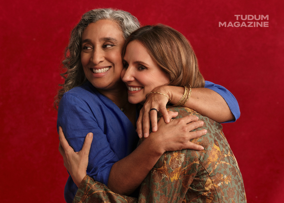 Geeta Gandbhir hugs Petra Costa as they stand against a red backdrop.