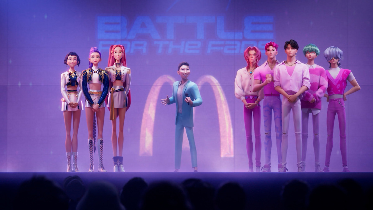 Animated characters stand on a brightly lit stage, divided into two groups, with a host in the center. They face an audience, under a "Battle of the Fans" sign, creating a competition atmosphere.