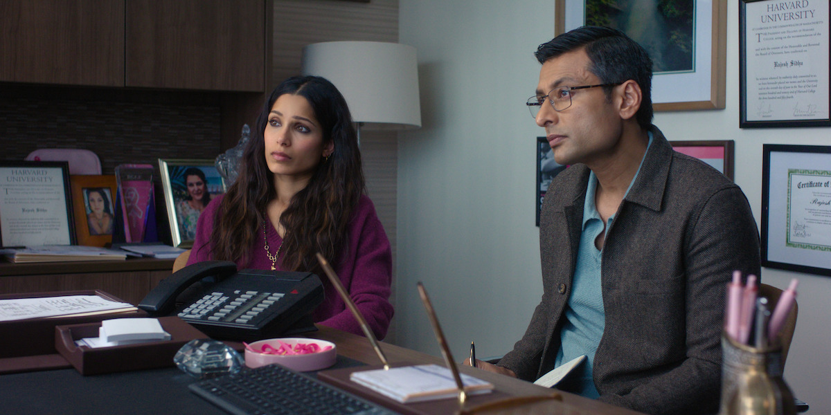 Two people sit at an office desk, surrounded by paperwork, office supplies, and framed certificates on the wall, suggesting a professional setting like a counseling or consultation session.