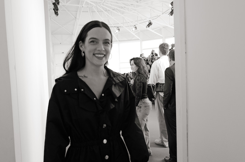 Riley Keough smiles in a black jacket.