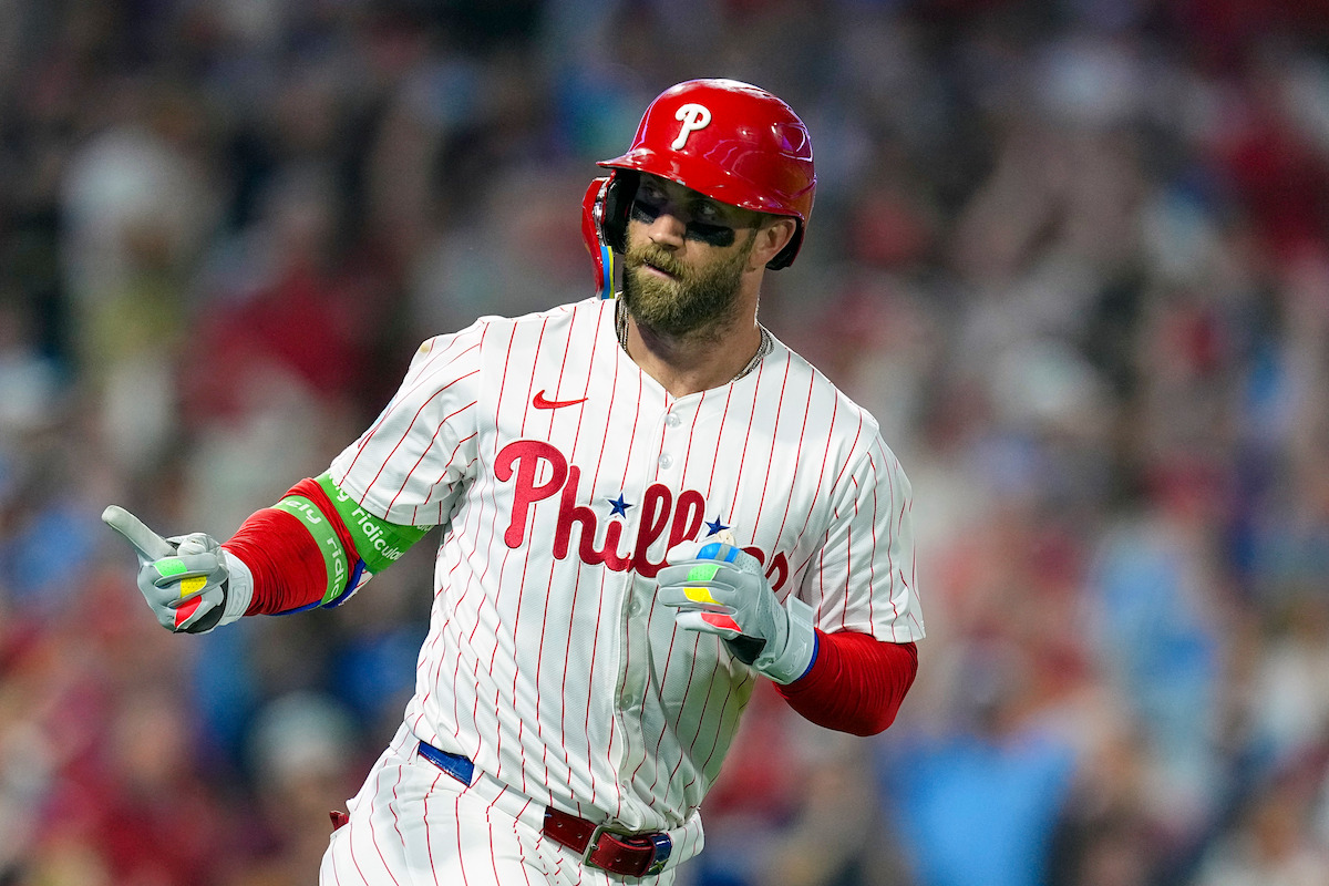 Philadelphia Phillies baseball player in pinstripe uniform and red helmet celebrates during a night game, crowd in background, energetic and focused mood.