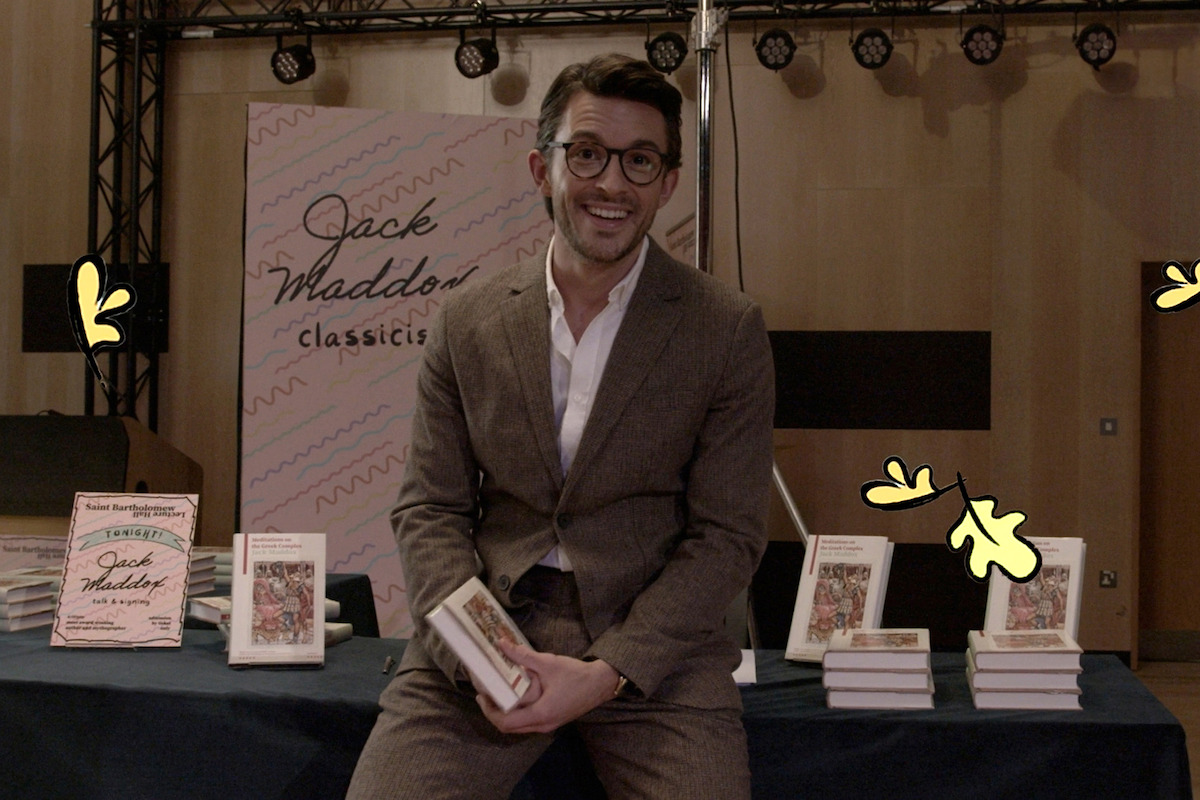 Jonahtan Bailey as Jack Maddox sits on a desk with book in Season 3 of ‘Heartstopper.’