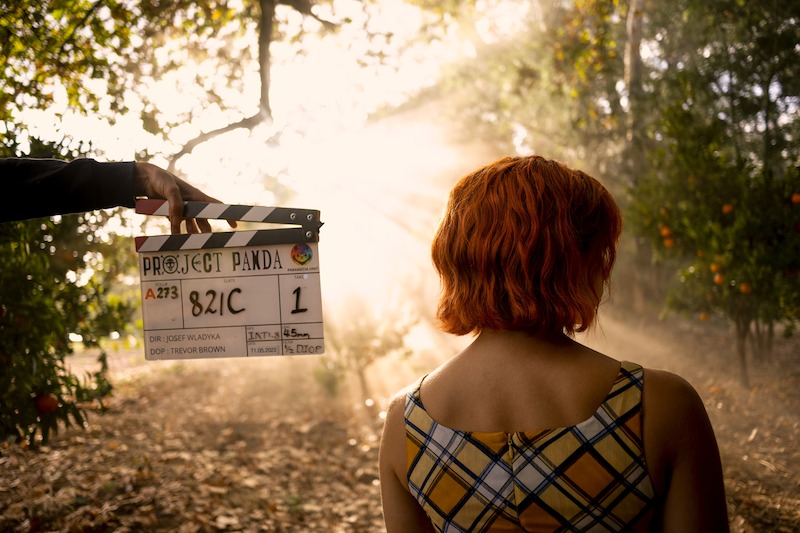  Emily Rudd as Nami stands with her back turned to the camera with a clapboard next to her in Season 1 of 'One Piece.'