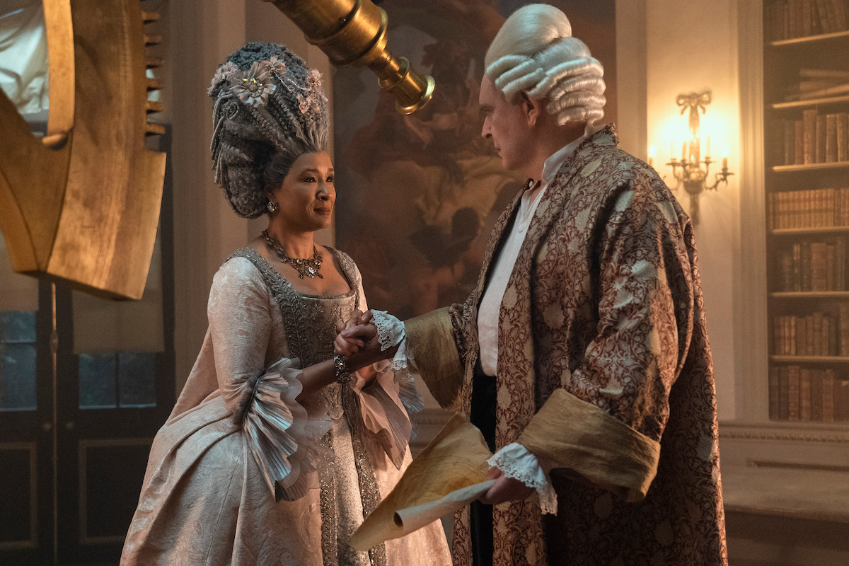 Golda Rosheuvel as Queen Charlotte and James Fleet as King George hold hands near a large telescope in Season 1 of ‘Queen Charlotte.’