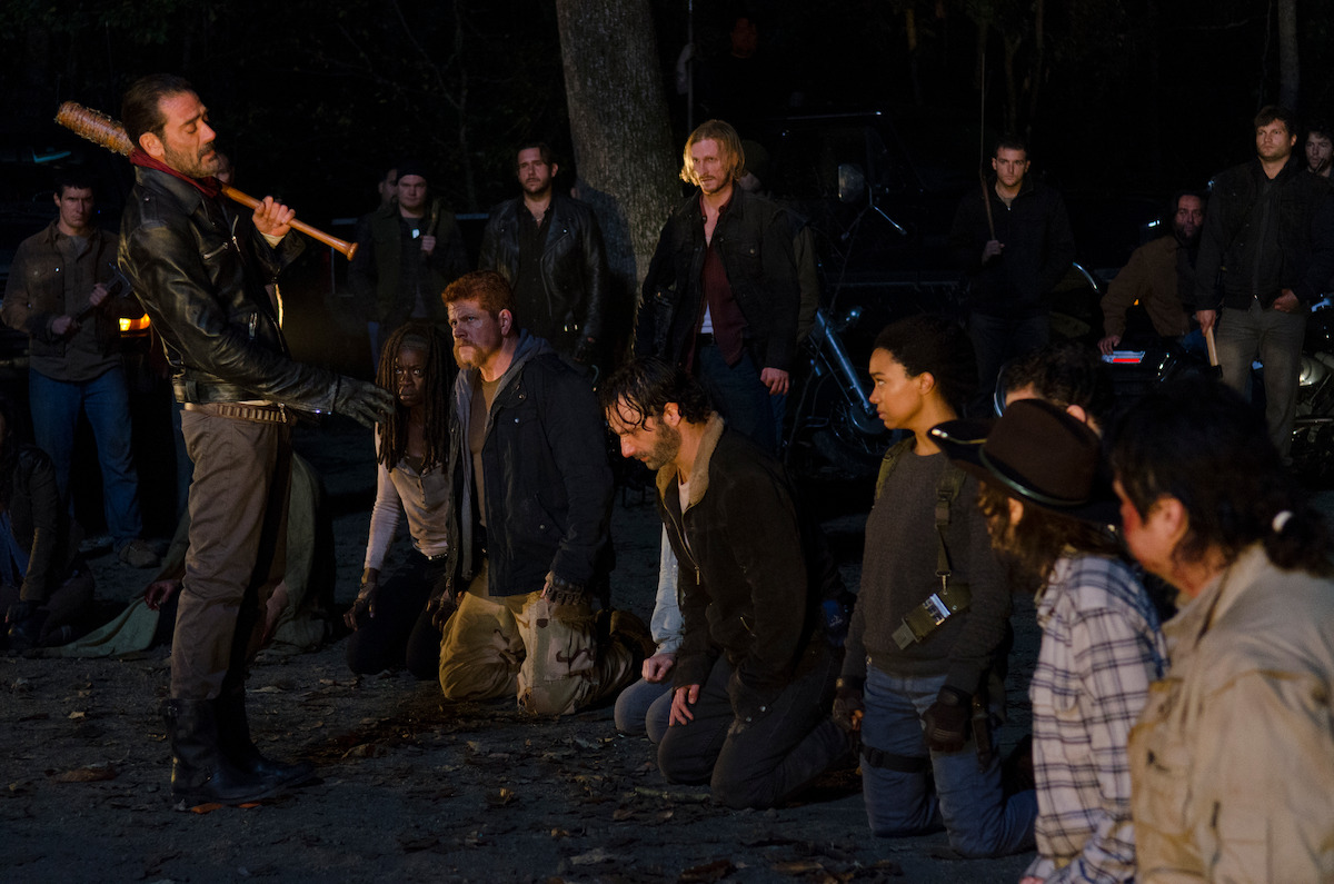 Negan stands over Rick and the gang holding his barbed wire baseball bat. 