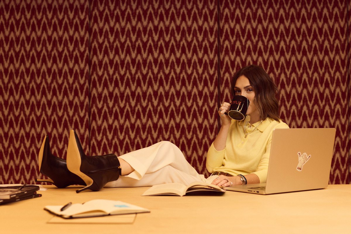 Atriz Isabelle Drummond segura uma caneca e posiciona os pés em cima de uma mesa de escritório