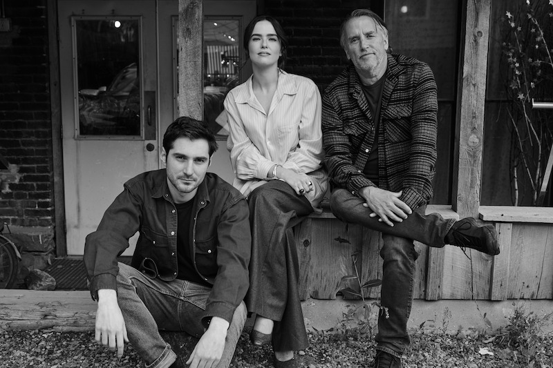 Guillaume Marbeck, Zoey Deutch, and Richard Linklater pose while seated next to each other on a porch.