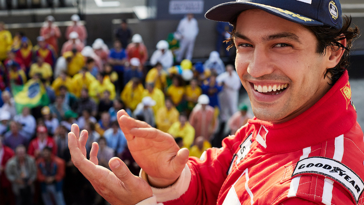 Gabriel Leone as Ayrton Senna smiles and claps his hands in front of a crowd in Season 1 of 'Senna'